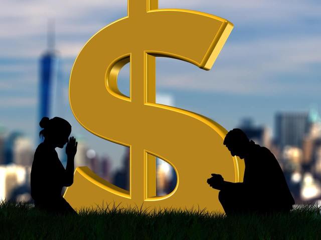 Two shadows of people kneeling in prayer beside a giant golden dollar sign