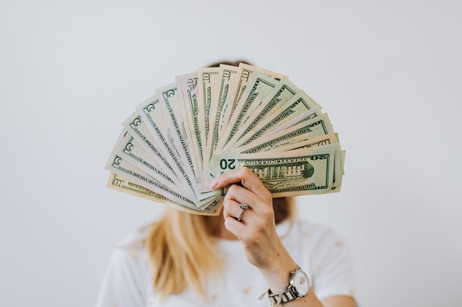 blond woman hiding face behind money